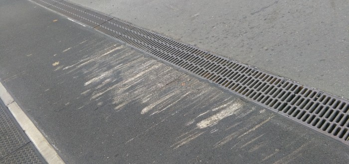 Vydřený asfalt od podvozků aut u odvodňovacího žlabu