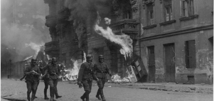 Příslušníci SS před hořící budovou. Německé jednotky během povstání vypalovali úkryty, stanoviště varšavských židů. Popelem lehly i synagogy